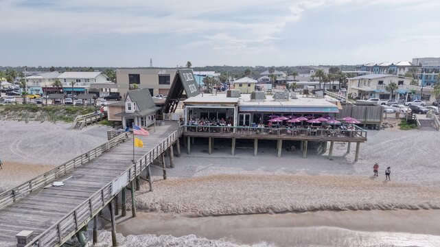 Aerial view of the Flagler Beach Pier with its wooden structure extending over the sand, featuring a restaurant with pink umbrellas, in Flagler Beach, Florida, United States.