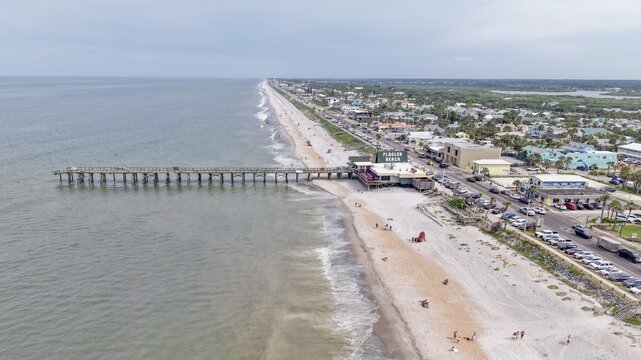 Aerial view of Flagler Beach Pier extending into the Atlantic Ocean, with the sandy coastline, coastal buildings, and parking area visible along the shore in Flagler Beach, Florida, United States.
