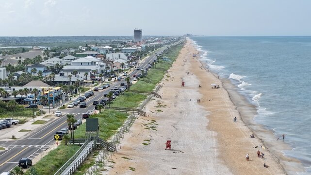 Aerial view of the coastline at Flagler Beach featuring a sandy shore, the Atlantic Ocean, a coastal road with parked cars, and beach houses in Flagler Beach, Florida, United States.