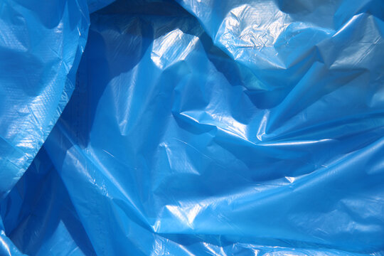 Crumpled blue texture of cling film, polyethylene film close up photo, art project, design background. Dangerous material for the environment concept