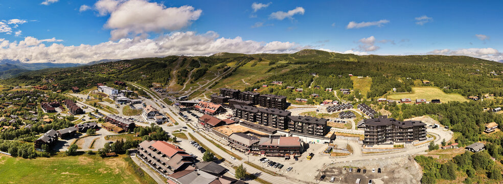 Aerial view of the village of Beitostolen with its modern wooden buildings, ski slopes, and surrounding lush green mountain landscape in Beitostolen, Innlandet, Norway.