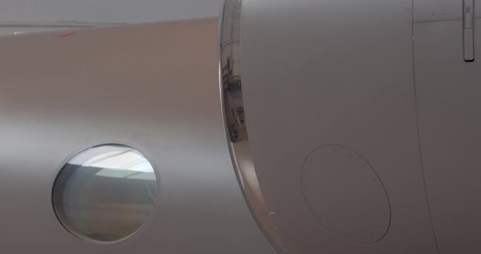 Small porthole window near engine fairing closeup showing circular glass, surrounding fairing and smooth fuselage during structural inspection and alignment check. Emphasis on fit,