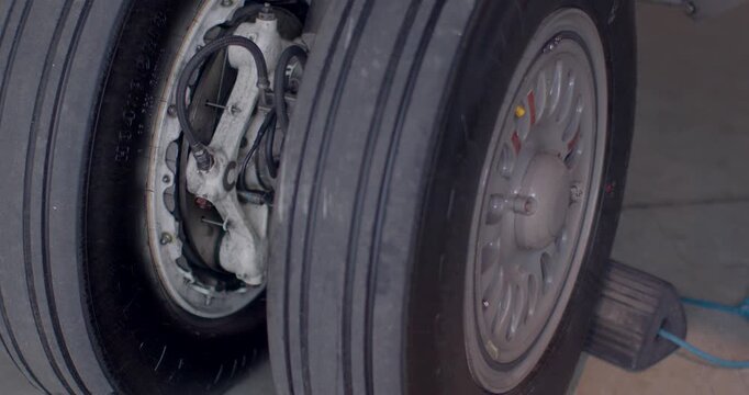 Landing gear wheel and tire closeup showing tread, rim and brake assembly with chock in foreground implying ground mechanic maintenance and safety procedures in hangar