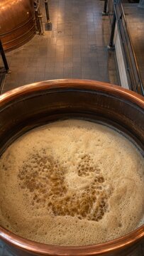 Copper fermentation tank filled with bubbling beer, showcasing the brewing process in a modern brewery with polished floors and industrial equipment in the background