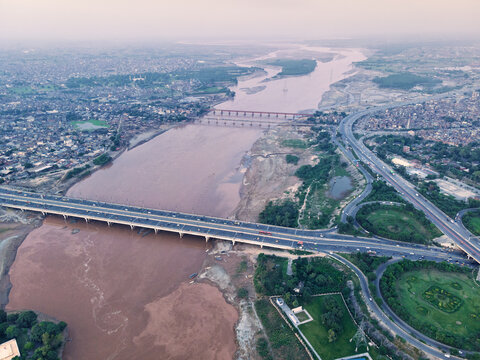 Aerial view of the Ravi River flowing through Lahore, featuring a prominent bridge, surrounding urban infrastructure, and lush green spaces in Lahore, Punjab, Pakistan.
