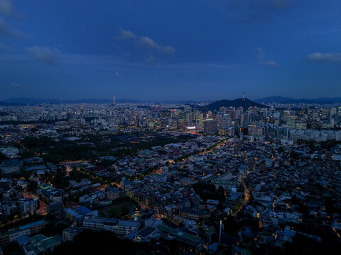 Aerial view of the Seoul skyline at night, featuring N Seoul Tower, illuminated streets, dense urban buildings, and a deep blue twilight sky in Seoul, Seoul, South Korea.