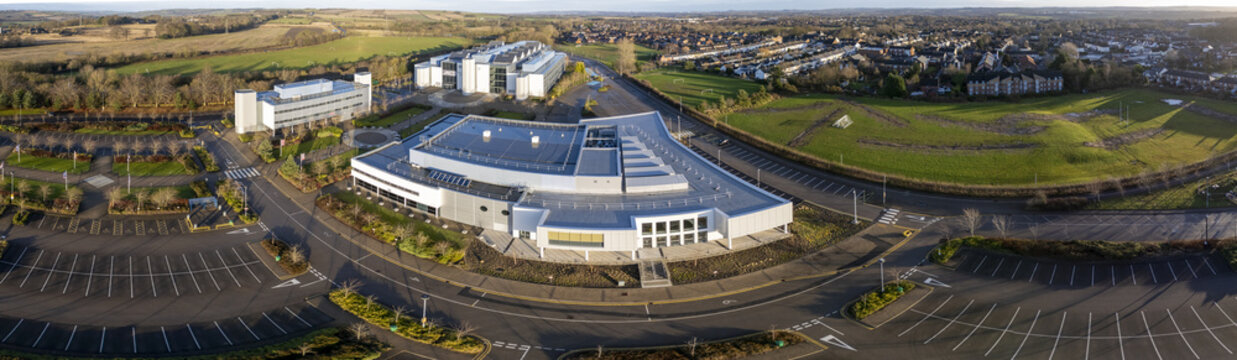 Aerial view of New College Durham University educational establishment complex with expansive parking lots, surrounded by green fields and residential areas in Durham, England, United Kingdom.