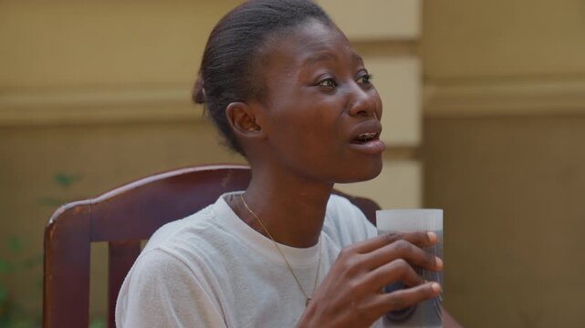 Intimate coffee date pause, black woman sipping drink, smiling and listening, patio chair, small cup, relaxed posture, warm tones, conversational rhythm, partner role, gentle laughter, candid
