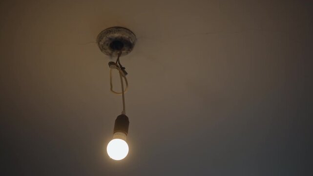 Cozy glowing ceiling. Peaceful scene of softly illuminated ceiling with exposed wiring. Serene domestic setting featuring warm hanging bulb with cracked plaster nearby and gentle shadow play