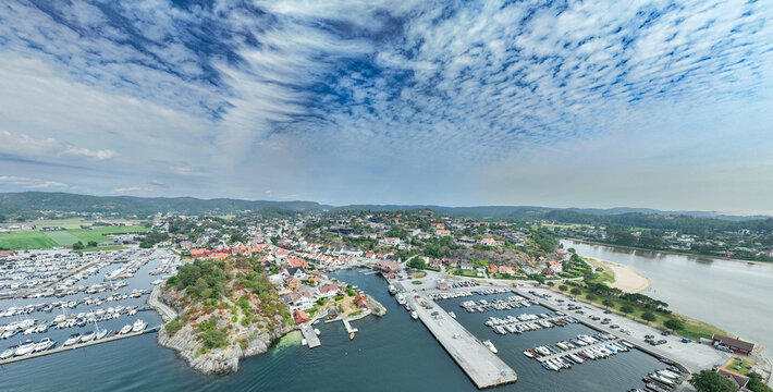 Aerial view of Hollen harbor with numerous boats docked at the marina, surrounded by coastal houses, rocky terrain, and calm blue waters in Holleheia, Agder, Norway.