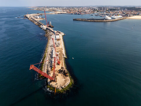 Aerial view of heavy-duty lattice-boom crawler cranes working on a breakwater construction project extending into the Atlantic Ocean near the harbor of Matosinhos, Porto District, Portugal.