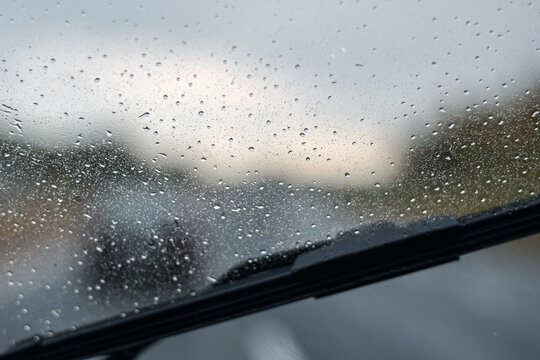Close-up view of water droplet on windshield with black wiper blade at bottom on overcast day