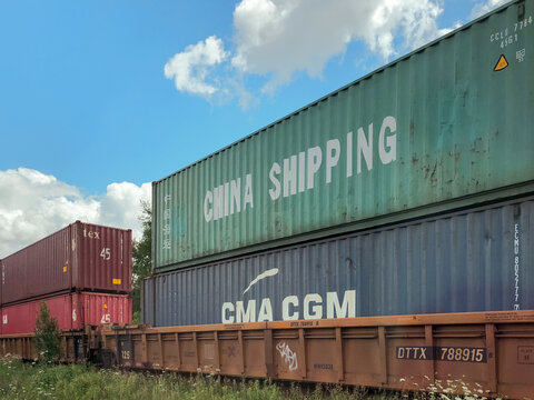 Low angle view showing stacked green China Shipping container and blue CMA CGM container on freight train car under blue sky, Ontario Canada 2020