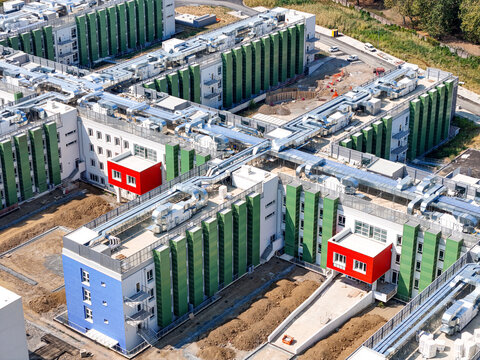 Aerial view of the New University Science Campus featuring modern buildings with green and red facades, rooftop ventilation systems, and ongoing construction, Grugliasco, Piedmont, Italy.