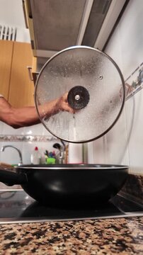 Slow motion video of a man's hand lifting a glass lid from a cooking pot, revealing steam and condensation from the hot meal, showcasing a healthy homemade vegetarian recipe preparation