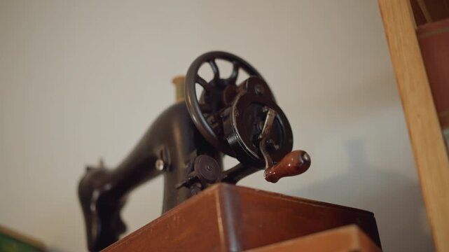 Antique sewing machine on wooden cabinet, visible hand crank and wheel, cast iron body with worn enamel, warm studio light, tailor workshop prop, heirloom decor, nostalgic craft mood