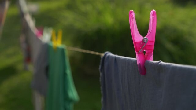 Pink clothespin on laundry line with hand removing clothes