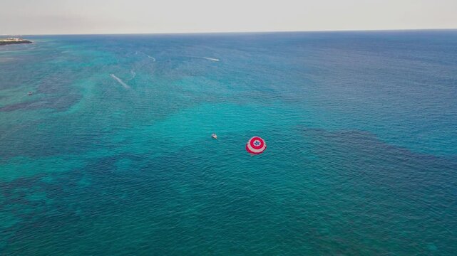 Aerial view of parasailing over the blue turquoise sea in Playa del Carmen. Drone shot of red parasail glidder soaring over Caribbean ocean in Riviera Maya, Mexico.