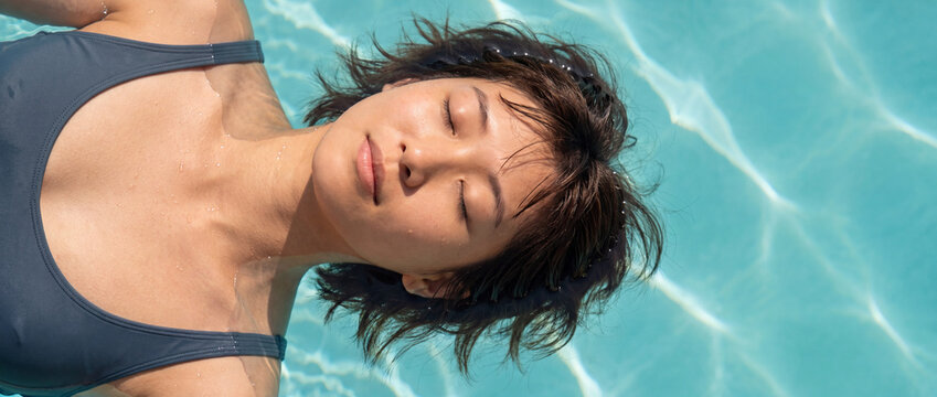 Woman floating in a swimming pool with eyes closed in sunlit turquoise water, capturing a serene peaceful moment for wellness, luxury spa, summer resort, and travel concept designs