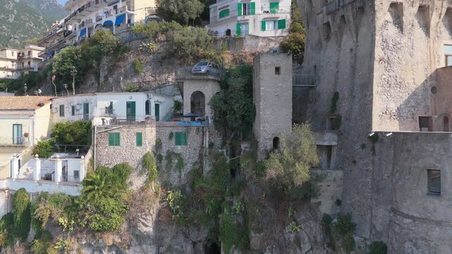 Aerial view of a rocky cliff face with a narrow cave entrance overgrown with lush green ivy and climbing plants along the rugged coastline in Cetara, Amalfi Coast, Italy.
