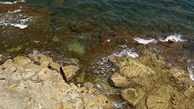 Rocky coastline with light brown limestone rocks and dark green sea water with small waves near the shore
