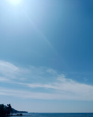 Obraz premium Blue ocean and sky meet at a distant horizon, with soft clouds and a small coastal landform creating a calm vertical composition. Ideal to decorate phone screens, wellness content, mobile background. 