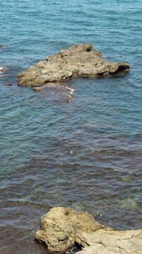 Vertical view of rock formations in deep blue sea water along rocky coastline on a sunny day