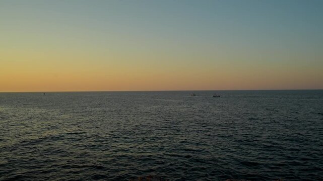 Calm dark sea surface stretching to horizon under clear gradient sky at dusk with warm orange glow
