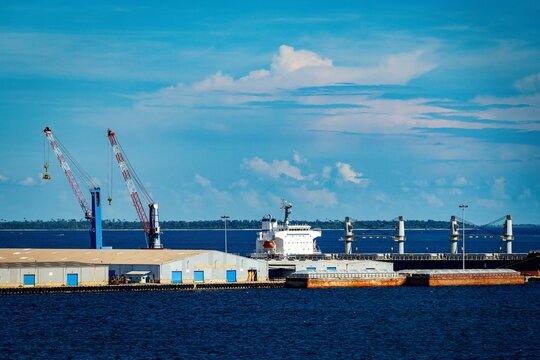 Cargo ship docked at industrial port with cranes and warehouses