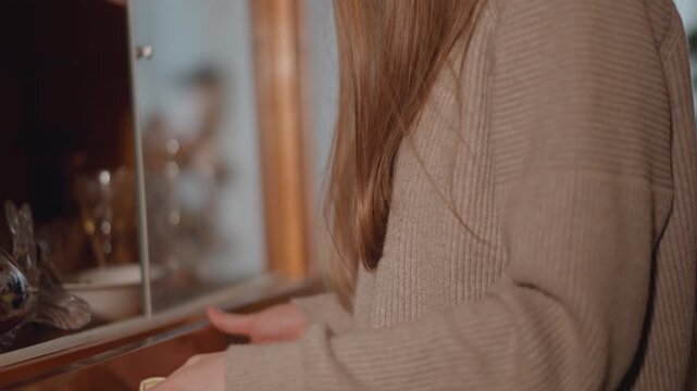 Caucasian woman inspects antique drawer contents with careful hands, closeup of gentle touch on cloth and glass shelves, focused expression in soft amber light, domestic ritual of sorting collectibles