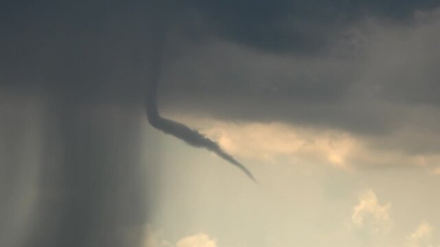Dissipating tornado funnel fades beneath storm clouds during dramatic meteorological event.