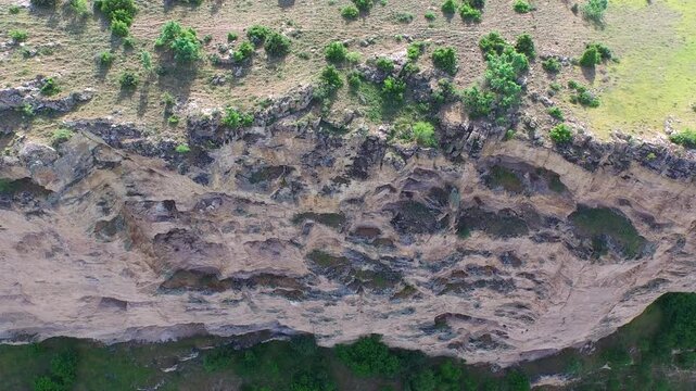 Aerial view reveals vertical karst cliff, limestone wall, and eroded rock layers near canyon.