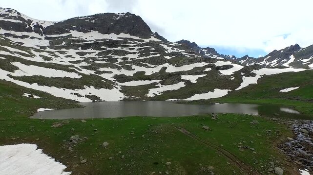 Aerial view of alpine mountain lake surrounded by melting spring snow and rugged peaks.