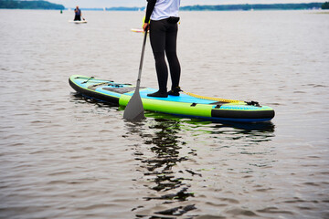 Active person paddleboarding alone on a calm lake. Individual enjoying stand up paddleboarding on a peaceful summer day. Solitary paddler standing on an inflatable SUP board. © Rabizo Anatolii