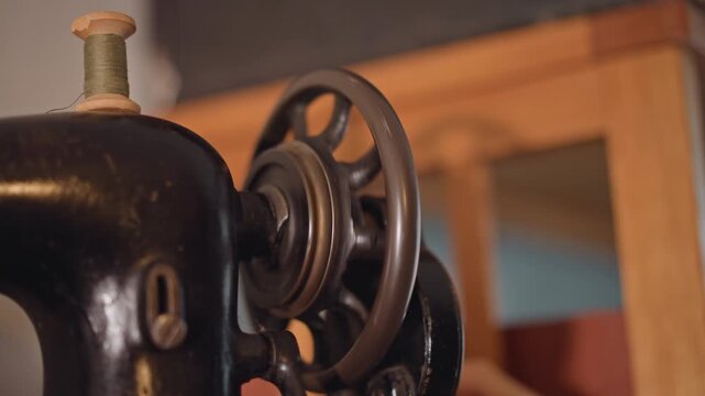 Adjusting thread on antique machine. Closeup of woman adjusting vintage sewing machine wheel and thread. An elderly woman delicately repairs historic black sewing device with wooden background