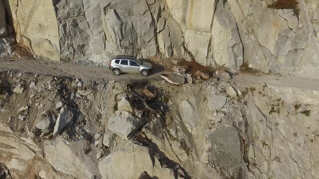 Aerial view of stranded 4x4 SUV on dangerous mountain road blocked by landslide near cliff.