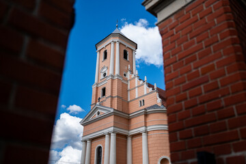 Klimatyczny różowy kościółek otoczony ceglanym murem na tle błękitnego nieba powitego nielicznymi chmurami w porze letniej w zachodniej Polsce © mbugajsky