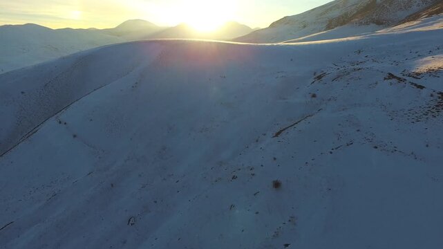 Drone view shows the winter sun setting over vast snowy Antarctic mountains and glaciers.