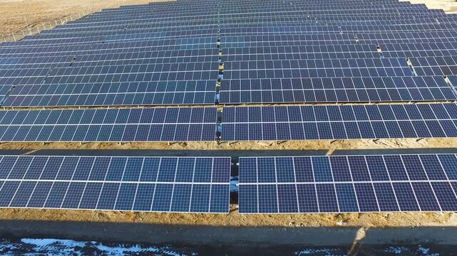 Aerial drone view of solar panels generating electricity above patchy snow in cold winter climate.