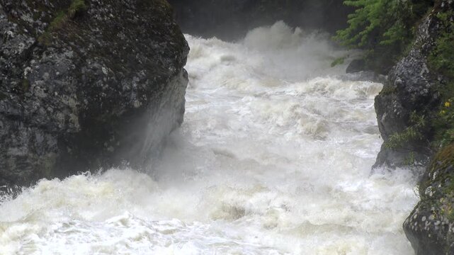 Super slow motion flood river surges through a mountain stream with raging white water and foam.