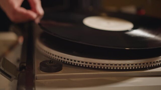 Closeup record placement on turntable, hands lowering vinyl onto platter, careful cueing motion in dim studio, vintage aesthetic, warm tones, tactile setup by hobbyist preparing playback.