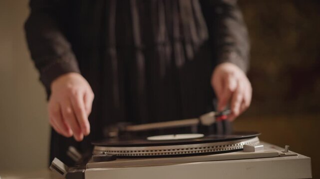 Hands cueing vinyl on turntable, dim room bokeh and warm tones set intimate performance vibe, precise finger placement and measured preparation for rhythmic playback and DJ practice.