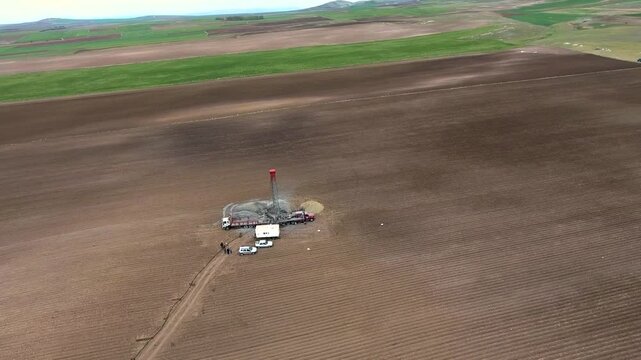 Aerial view shows a drilling rig extracting groundwater from a flat alluvial plain farmland.