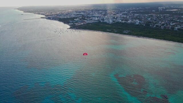 Aerial view of parasailing over the blue turquoise sea in Playa del Carmen. Drone shot of red parasail glidder soaring over Caribbean ocean in Riviera Maya, Mexico.