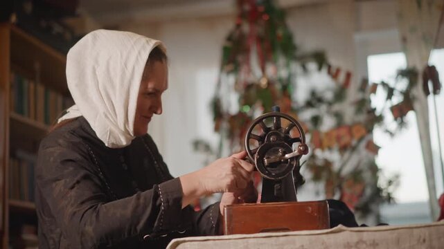 Senior woman sewing. Elderly lady mending fabric softly. Older woman fixing cloth beside festive tree illumination. Aging woman carefully stitches material near decorated holiday tree