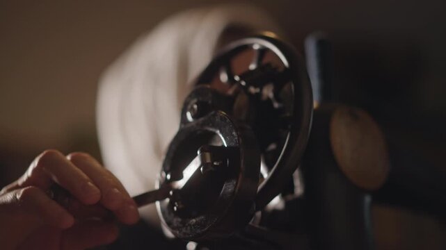 Focused woman gently adjusting historic sewing apparatus under warm glow. Careful woman with headscarf diligently repairing vintage sewing machine using screwdriver in warm lighting environment