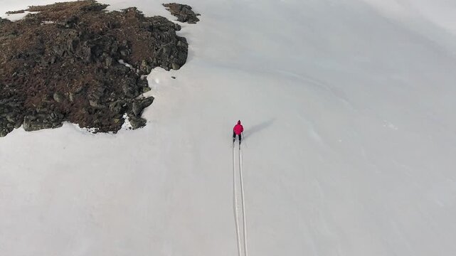 Solo skier in red jacket crossing pristine snow on mountain slope during winter adventure.