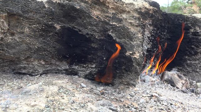 Flame of burning methane gas emerging from underground rock crack in geological formation.