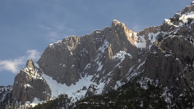 Rocky peak rising through clouds on snowy high mountain wall in the Rocky Mountains of America.