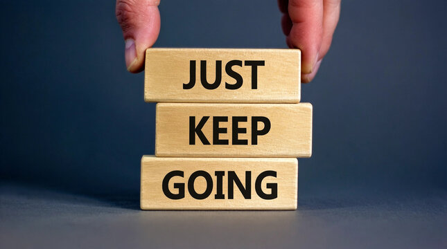 Hand stacking wooden blocks with motivational phrase 'Just Keep Going' for perseverance and resilience concept